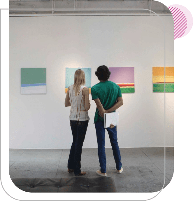 Two people looking at paintings in a room.